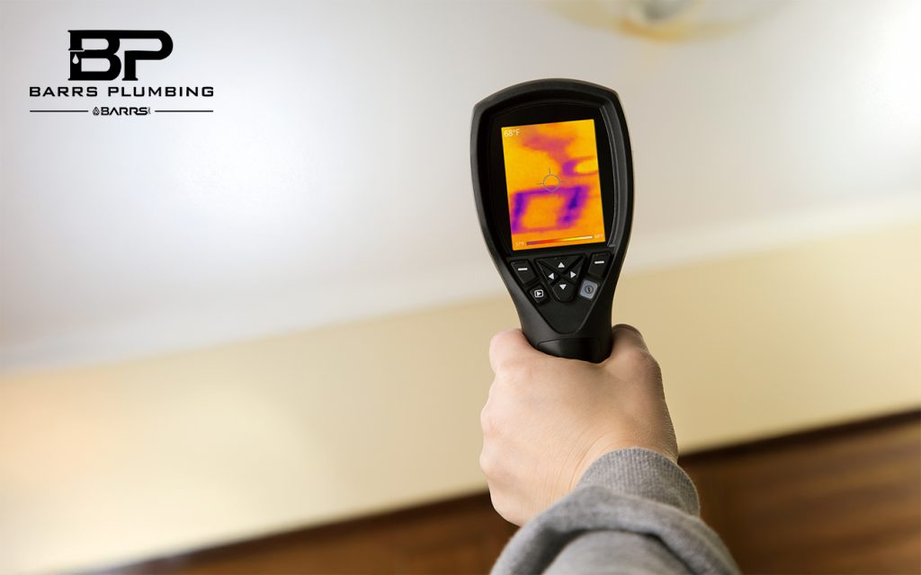 A homes ceiling with a leaking pipe and inspector looking at water damage through a thermal imaging camera.